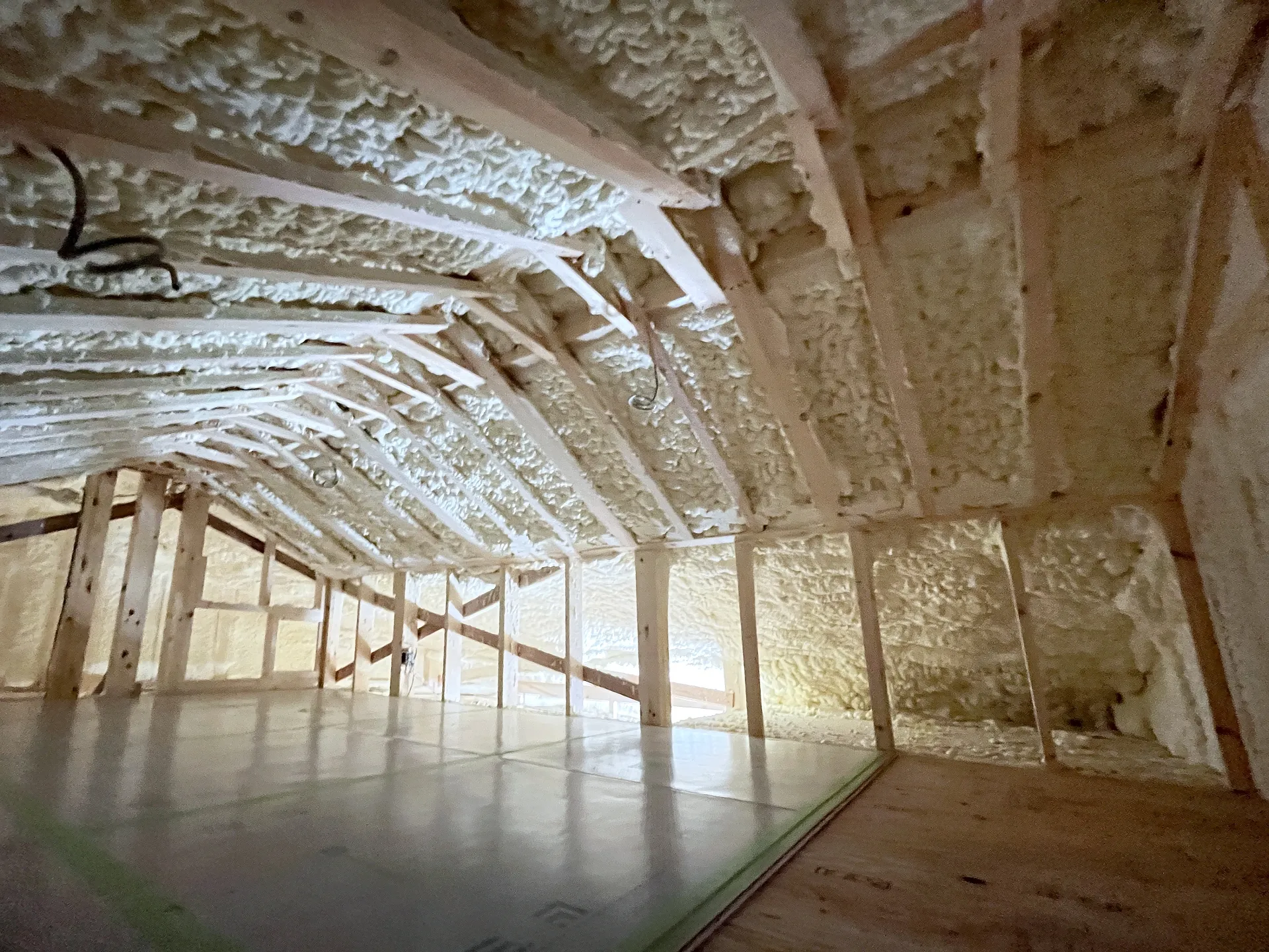 建築中の住宅の屋根裏。垂木と壁の間に吹付けの断熱材が隙間なく施工され、床は養生された合板