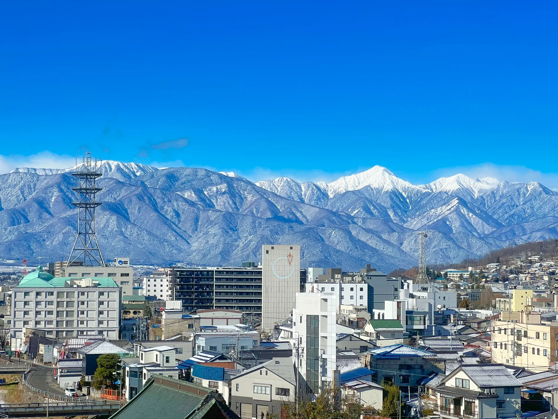 雪をいただく北アルプスの山並みを背にした、長野県の市街地