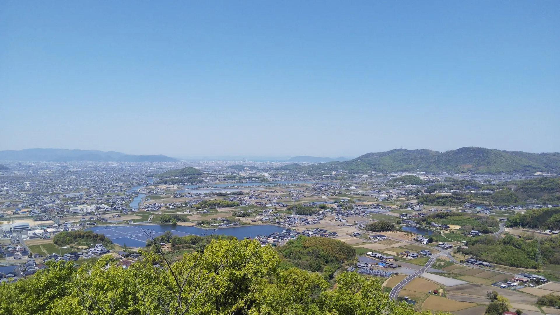 高台から望む讃岐平野の眺め。ため池と田畑の間に市街地が広がり、遠景に低い山並みが連なる