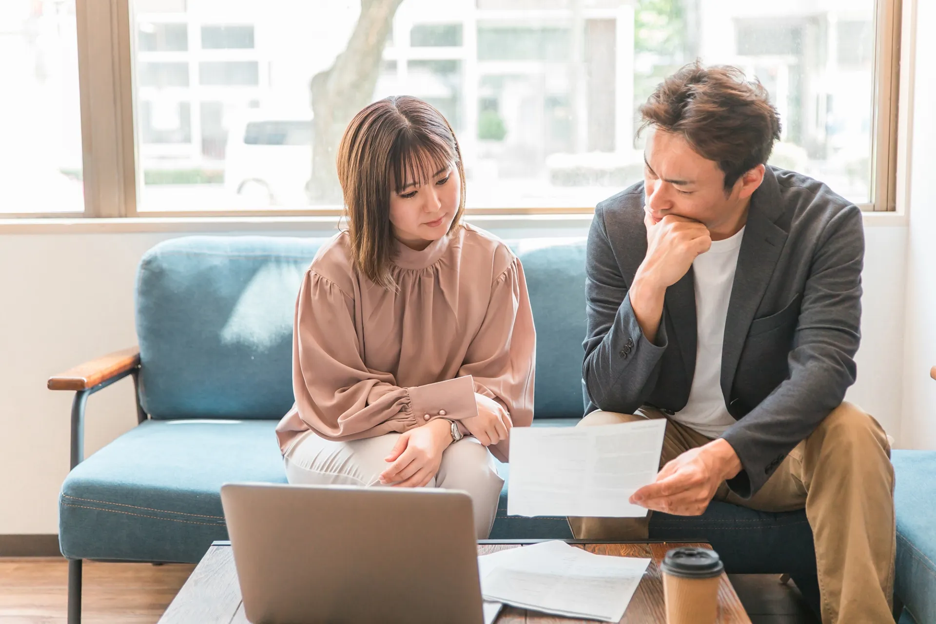 ソファに座り、届いた資料とノートパソコンを見ながら家づくりを検討する夫婦
