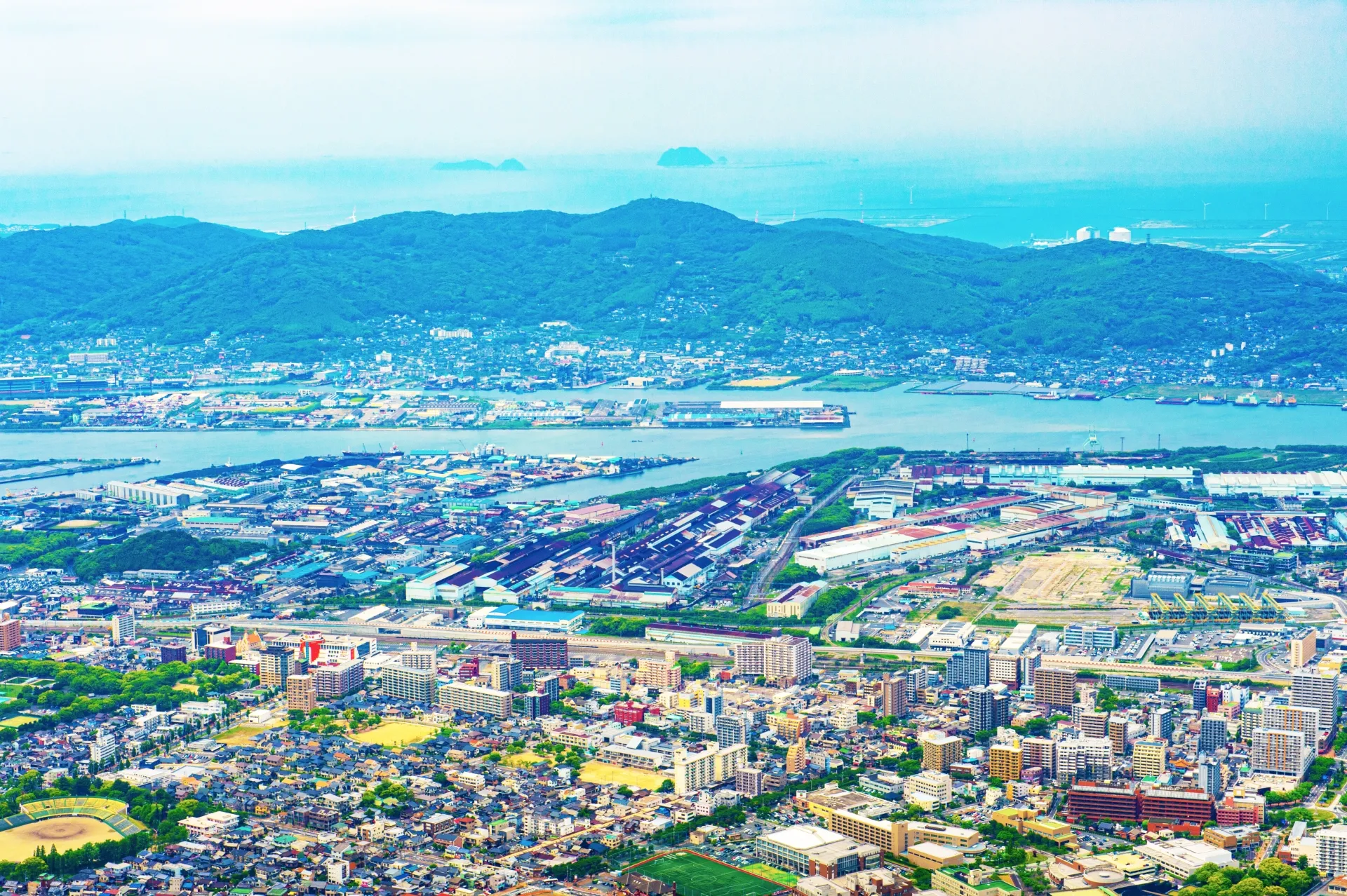 洞海湾をはさんで工場地帯と住宅街が広がる北九州の眺めと、遠くに見える響灘